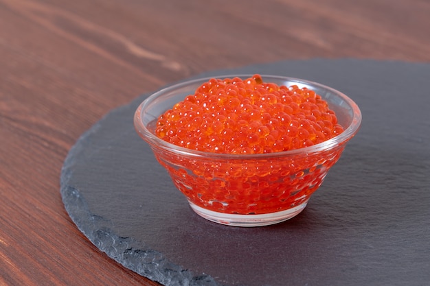 Red caviar in the glass jar on the dark brown wooden table