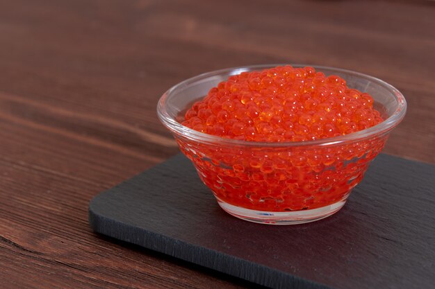 Red caviar in the glass jar on the dark brown wooden table