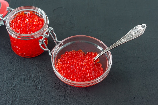 Red caviar in glass jar with silver spoon . Sea food. Healthy eating. Diet. black background.