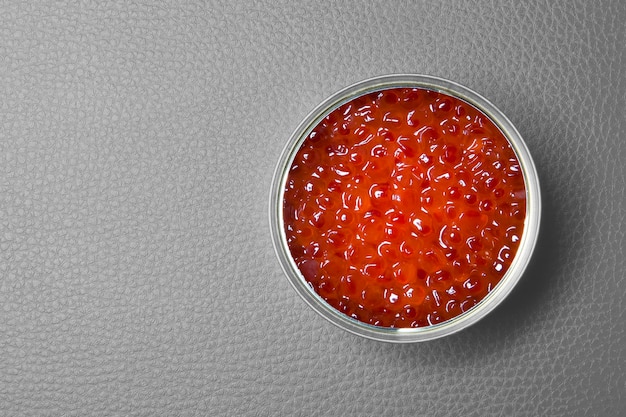 Red caviar in the open tin can on a gray background