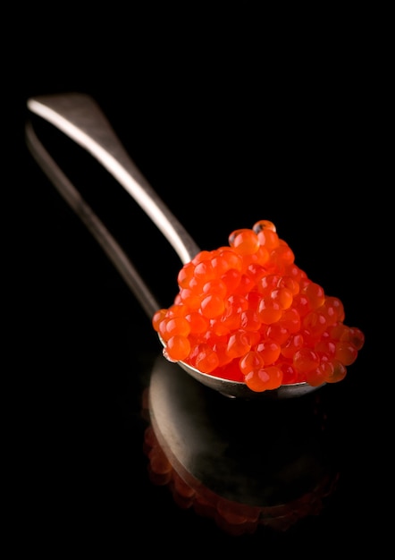 Red Caviar in a spoon over black surface. Close-up salmon caviar. Delicatessen. Gourmet food. Texture of caviar. Seafood