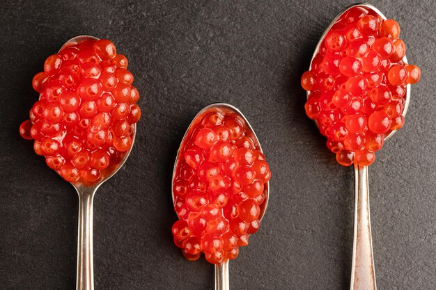 Photo red caviar in three spoons on a black background. salmon caviar close-up. delicacies. delicious food. the texture of caviar. seafood