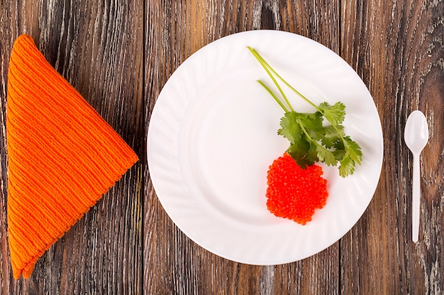 Red caviar on a white plate with herbs on wooden surface