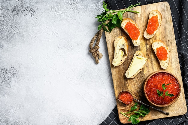 Red caviar in wooden bowl and sandwiches on cutting board. top view.