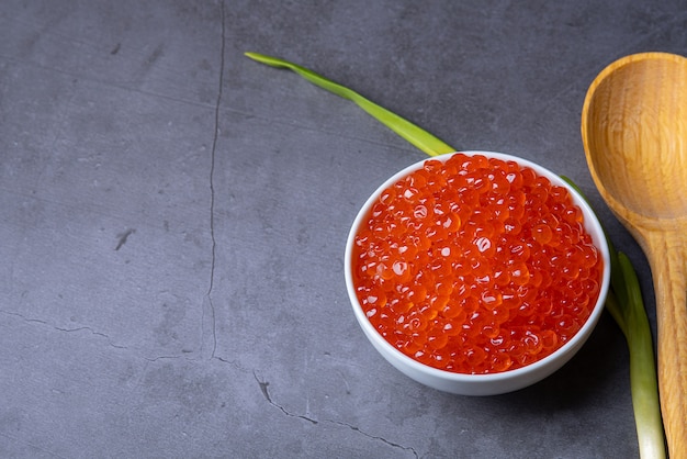 Red caviar in a wooden cup on a grey background with a spoon.