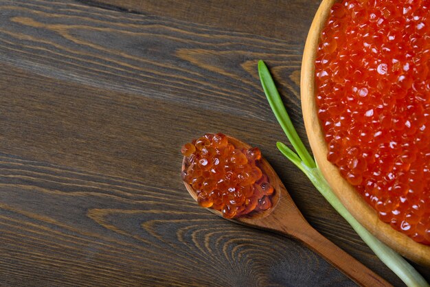 Red caviar in a wooden cup on a wooden background with a spoon.