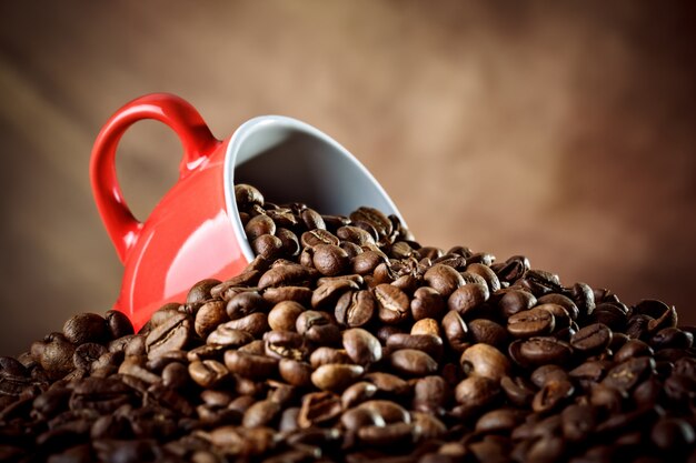 Red ceramic coffee cup lying in the coffee beans