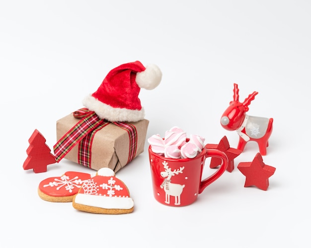 Red ceramic cup with drink and marshmallows, near baked christmas gingerbread, white background