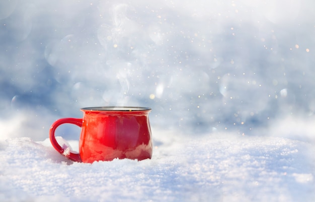 Red ceramic cup with hot tea stands on the snow on a sunny day the background is out of focus