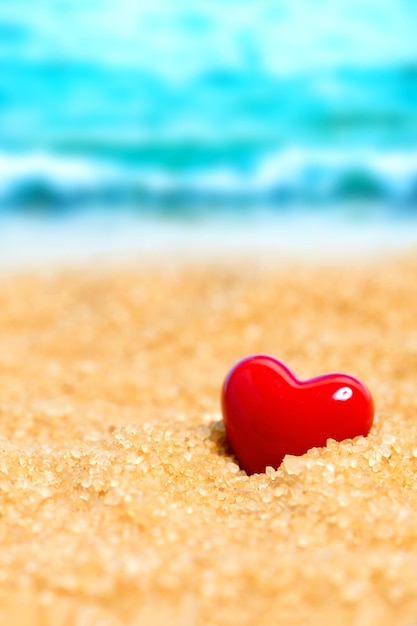 Red ceramic heart in the sand on the background of beach and sea