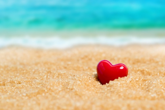 Red ceramic heart in the sand on the background of beach and sea