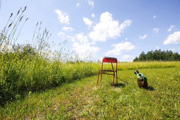 Red chair and watering can on mown green summer meadow in countryside.