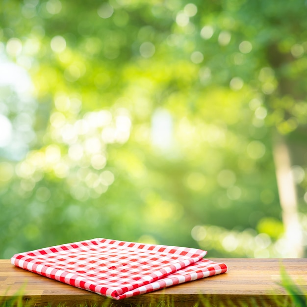 Red checked tablecloth on wood with blur green bokeh of tree