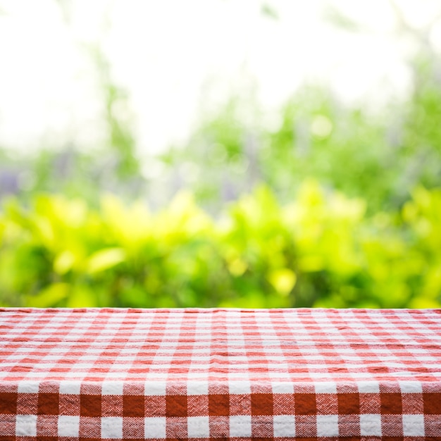 Red checkered tablecloth texture top view with abstract green from garden background.For montage product display or design key visual layout.