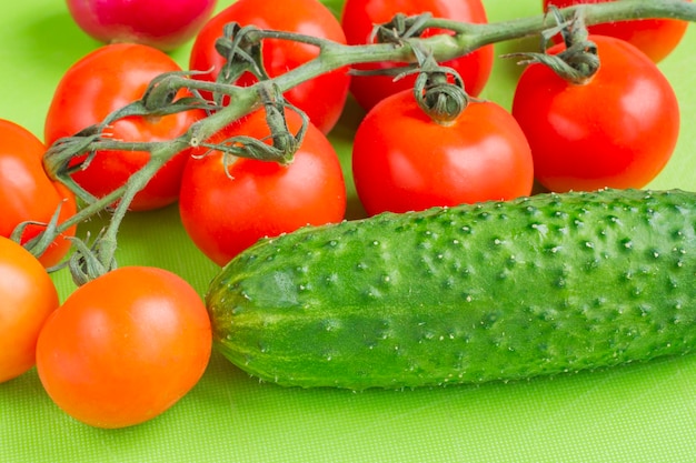 Red cherry and green cucumbers on green cutting board