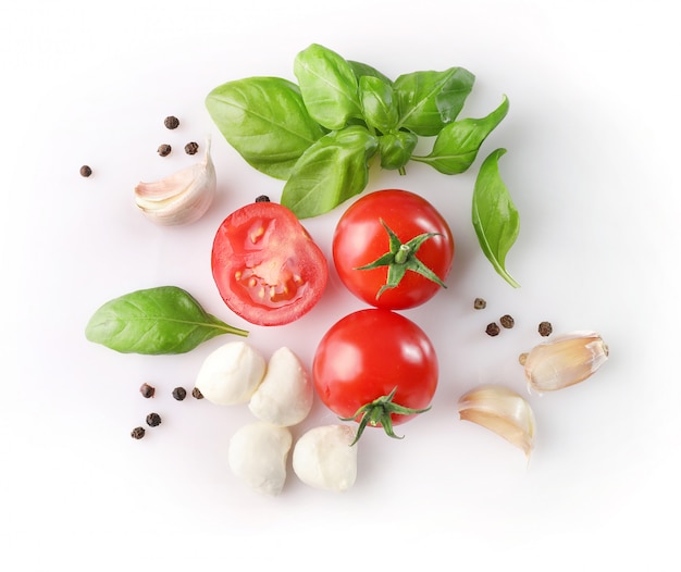 Red cherry tomatoes, basil, and mozzarella on white background