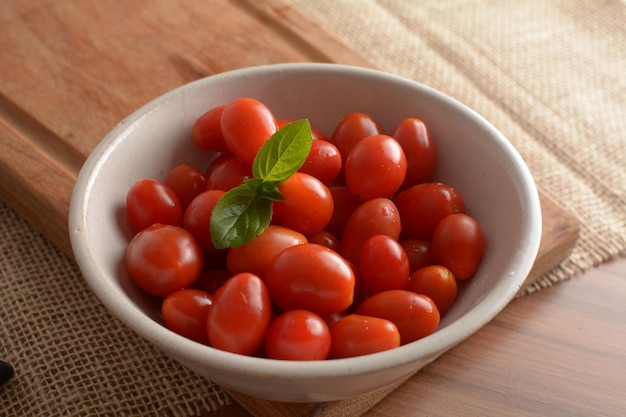 Red cherry tomatoes in a white bowl on a wooden table