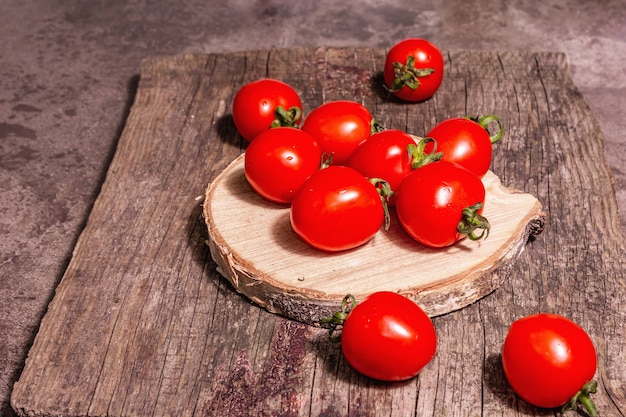 Red cherry tomatoes on a wooden stand. Fresh sweet vegetables, organic farmer product. Modern hard light, dark shadow, chopping board, marble stone background, copy space