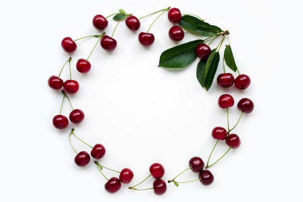 Фото Красная вишня с черешками, выложенными в раму с зелеными листьями. понятие о вегетарианстве и любви к природе. фруктовая рамка. фруктовая диета копии сохранить