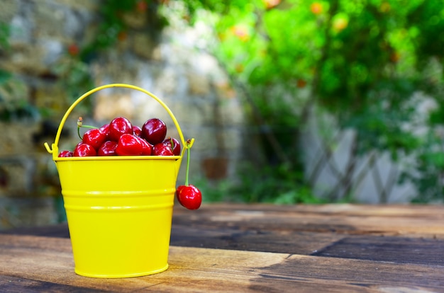 Red cherry in a yellow bucket on a brown wooden table