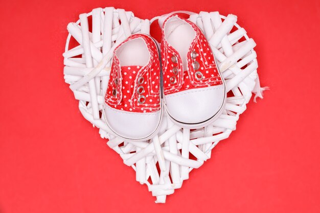 Red children's shoes with white polka dots on a decorative white heart.