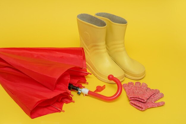 Red children's umbrella boots and gloves on a yellow background with copy space