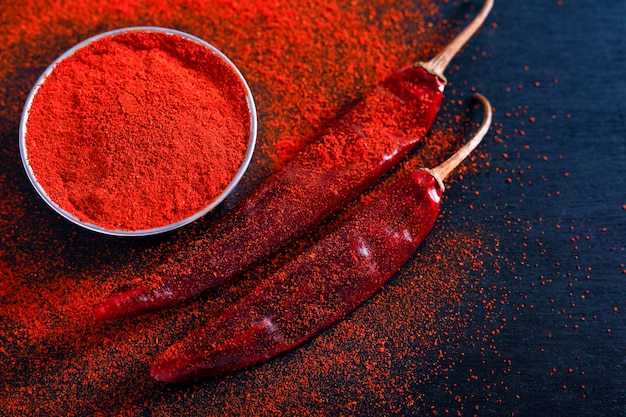 Photo red chili pepper flakes and chili powder burst on black background