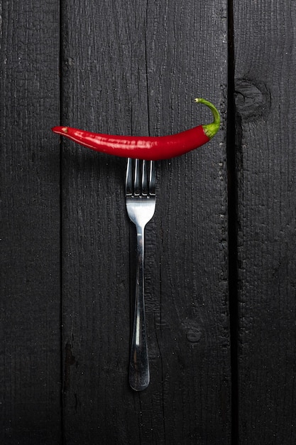 A red chili pepper on a fork on a black table