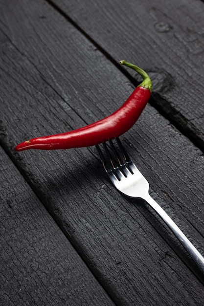 A red chili pepper on a fork on a black table