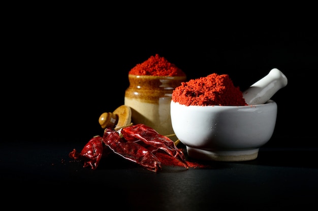 Red Chili Pepper powder in pestle with mortar and clay pot with Red Chili Peppers on black surface