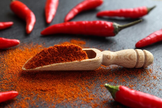 Red chili powder in wooden spoon and chili peppers close-up. Selective focus.