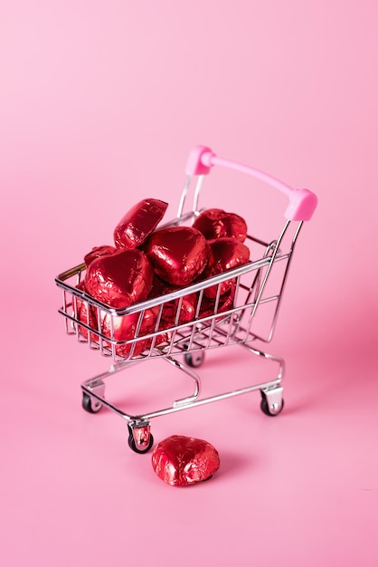 Red chocolate candy in shape of hearts in mini shopping\
cart