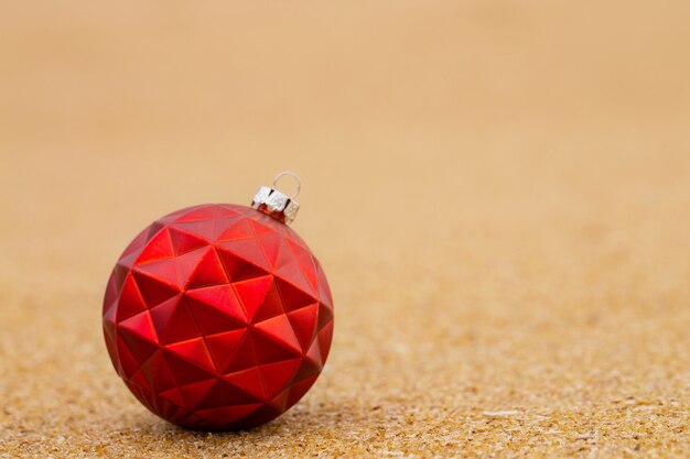 Red Christmas ball on the sandy shore of the ocean