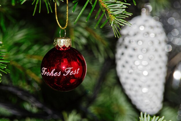 Red christmas ball with happy holiday text in german against blurred decoration