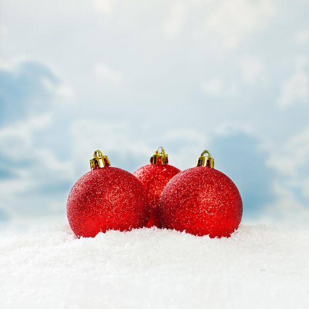 Red Christmas baubles on white snow background against blue sky with white clouds Winter holidays concept