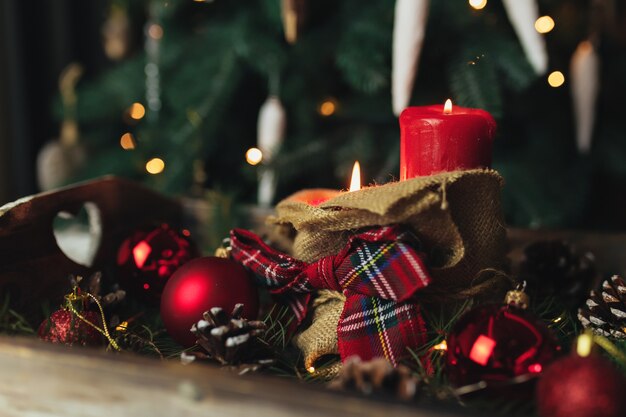 Red christmas decorations on the table at blurred christmas tree with candles . High quality photo