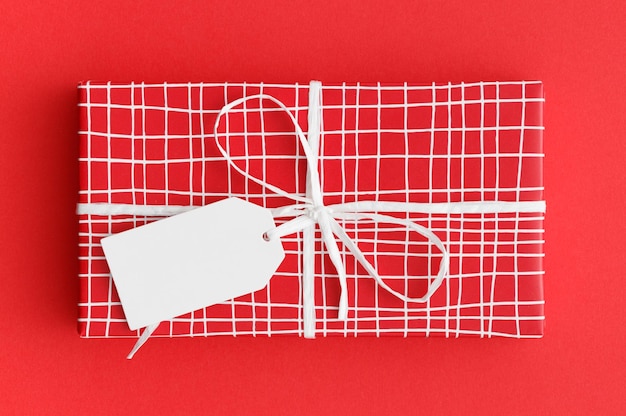 Photo red christmas gift with a blank tag mockup on a red background