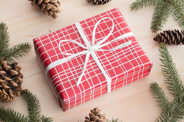 소나무 콘 잎과 나무 테이블에 꼬기로 둘러싸인 빨간 크리스마스 선물