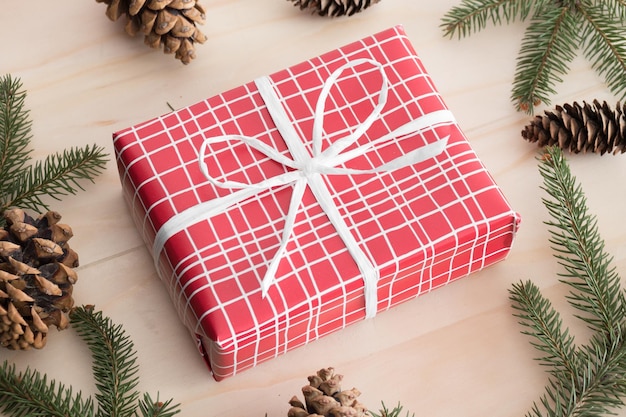 Red christmas gifts surrounded with pine cones leaves and twine on a wooden table