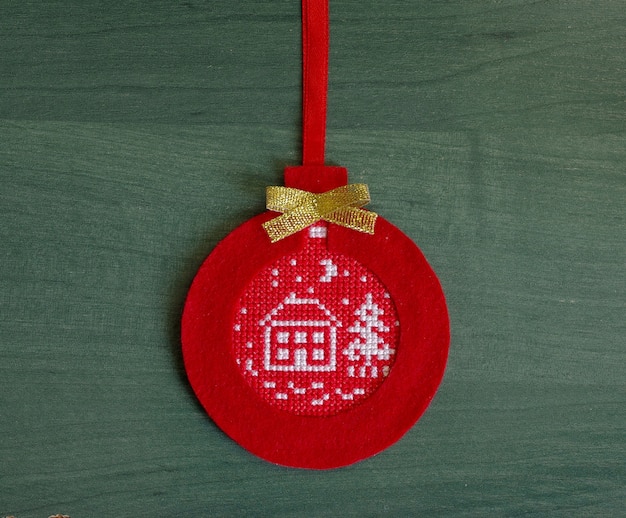 Red Christmas tree decoration made of felt with embroidered ornament on a green background