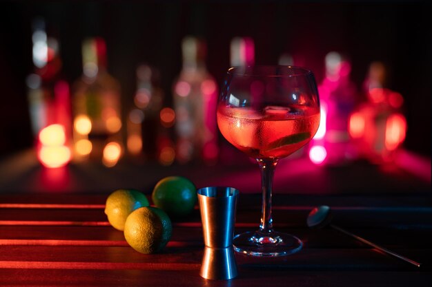 Foto bicchiere da cocktail rosso con lime e bottiglie bar illuminate