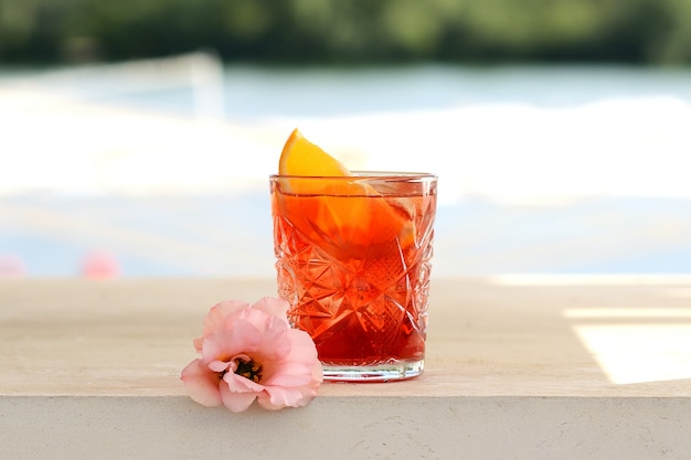 Red cocktail in a glass with a slice of orange. With flower decor