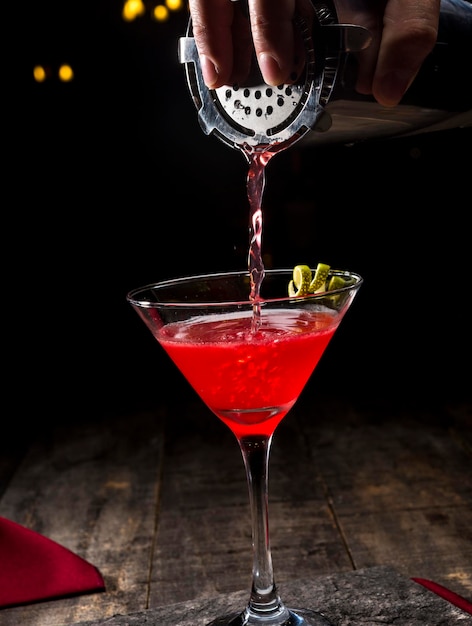 Red cocktail in a martini glass on a black background with a bartender