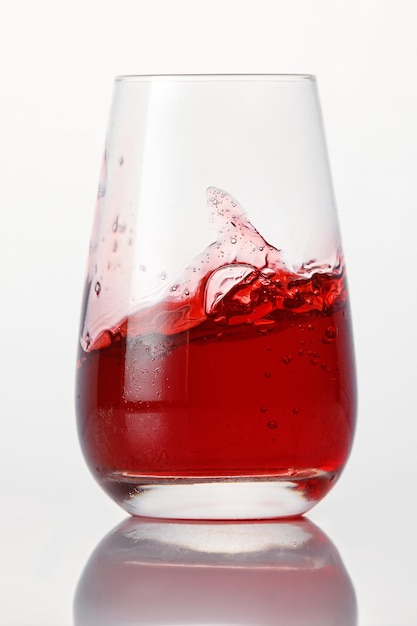 Red cocktail splashes in a glass on a white background