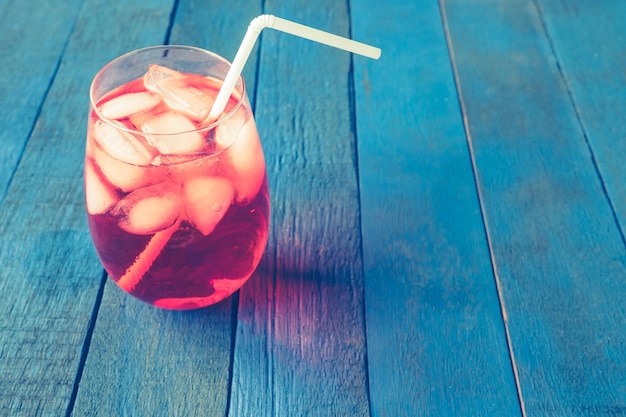 Photo red cocktail with ice cubes on blue painted wood plank background.