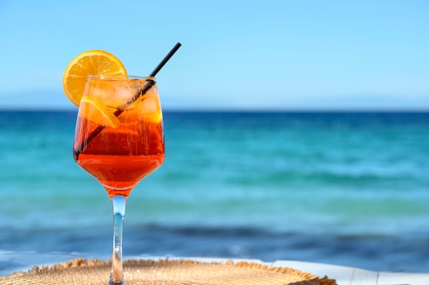 Red cocktail with orange slice and ice on a sea background