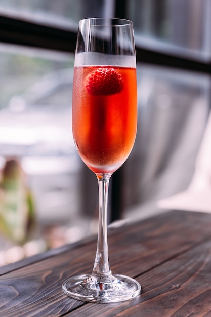 Красный коктейль с малиной внутри в стеклянном вине.