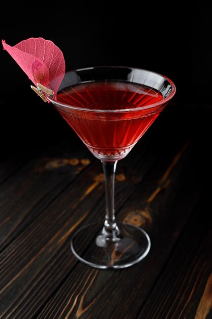Red cocktail with rose decoration in a martini glass on a dark wooden background