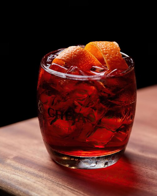 A red cocktail with a slice of orange on the rim sits on a wooden table.