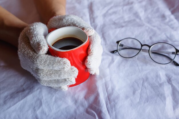 Tazza di caffè rossa in mano che indossa guanti in inverno